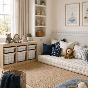 May include: A nursery room featuring a low floor mattress with patterned pillows, a wooden storage unit with blue and white gingham bins, a woven basket with a navy blue blanket, a blue rug, and a doll wearing a gray dress on the floor.