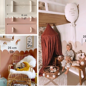 Op de afbeelding: Een babykamer met een witte commode met roze lades, een bruine rotan schommelstoel met een wit schapenvacht, een rode kap die aan het plafond hangt, een witte ballon met de tekst "Zoja 18.12.2021 3400g 51cm" en een houten bankje met een mand vol knuffels. De muren zijn lichtbruin geverfd met een gegolfde rand in een donkerdere bruine kleur.