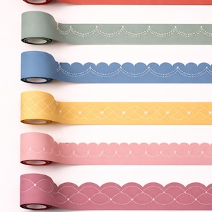 Könnte beinhalten: Eine Auswahl an dekorativen Washi-Tapes in verschiedenen Farben, darunter Rot, Grün, Blau, Gelb, Rosa und Burgunder. Jedes Tape zeigt ein einzigartiges Muster, wie Herzen, gepunktete Linien und gewellte Kanten. Die Tapes sind aufgerollt.