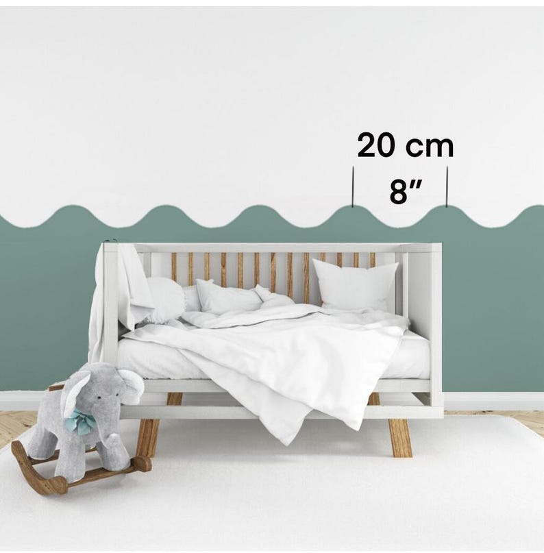 Op de afbeelding: Een wit babybedje met een wit matras en een grijs schommelpaard ervoor. De muur achter het babybedje is lichtgroen geverfd met een golvend lijnenpatroon. De tekst "20 cm 8" staat op de muur.