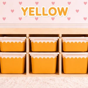 May include: A wooden storage unit with six yellow bins with white scalloped edges. The word "YELLOW" is displayed in orange letters above the unit. The background features a pink wall with heart patterns.