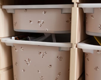 May include: A set of beige storage bins with white floral patterns. The bins are placed in a wooden shelf unit. The bins have a light beige color with a white floral pattern. The shelf is made of light-colored wood.
