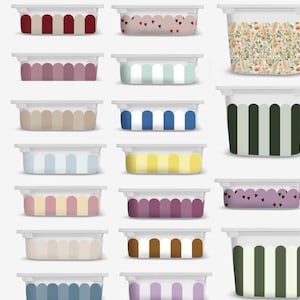 May include: A collection of rectangular plastic food storage containers with white lids. The containers feature various patterns including vertical stripes in red, blue, yellow, and green, scalloped edges, small heart prints, and a floral botanical design.