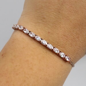 Puede incluir: Una pulsera de oro rosa con una fila de piedras de circonita cúbica ovaladas transparentes.