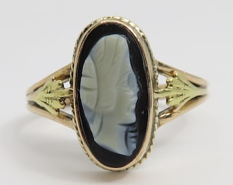 Op de afbeelding: Een gouden ring met een zwart-witte cameo met een profiel van een vrouw. De cameo is gezet in een gouden ovale lijst met een delicaat ontwerp.