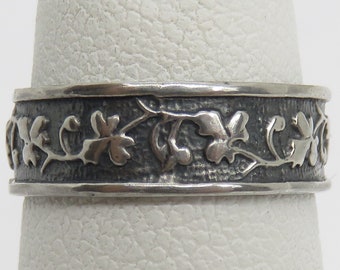 Puede incluir: Un anillo de banda de plata con un acabado texturizado y un delicado diseño floral. La banda es ancha y el diseño es intrincado.