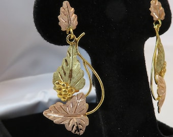Pode incluir: Um par de brincos de ouro com um design de folhas. Os brincos são feitos de ouro de 10 quilates e apresentam um cacho de folhas com um design de uva no centro.