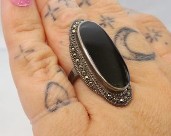 May include: A silver ring with a black oval gemstone surrounded by a border of small, sparkling stones.