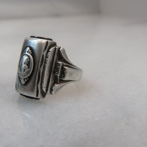 May include: A silver-toned ring with a rectangular face featuring a detailed relief of a woman's profile within a circular frame. The ring has a textured band and a classic, vintage design.