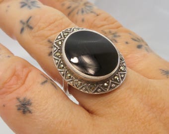 May include: A silver ring with a black oval gemstone surrounded by a border of small, sparkling stones.