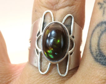 Op de afbeelding: Een zilveren ring met een grote ovale groene en bruine edelsteen, gezet in een decoratieve zilveren band.