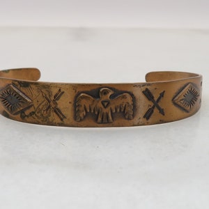 May include: A copper bracelet with an embossed design of a bird, arrows, and geometric shapes.