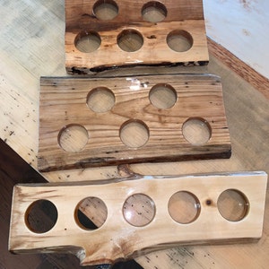 May include: Three wooden beer flight boards with six circular cutouts each. The boards are made from natural wood with a clear finish, showcasing the wood grain. The boards vary in color from light to dark brown, with live edges.