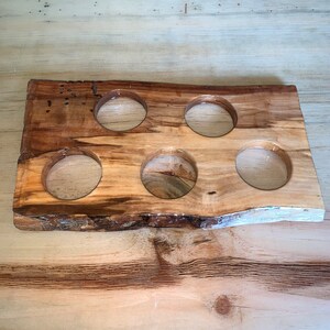 May include: A handcrafted wooden drink caddy with six circular openings. The caddy is made from a single piece of wood with a natural edge, showcasing the wood's grain and color variations. The caddy is designed to hold six glasses or small bottles.