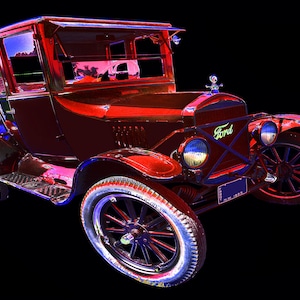 May include: A red vintage Ford Model T car with a black background. The car has a black top and a black license plate that reads "1927, N.M. 1862".