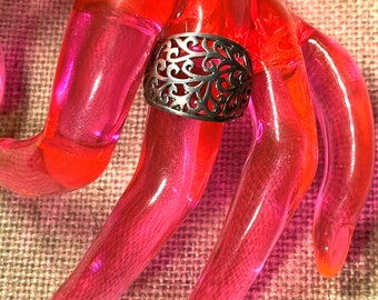 May include: A silver filigree ring with a delicate, intricate design. The ring is wide and has a rounded shape.