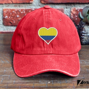 Könnte beinhalten: Rote Baseballkappe mit einem gestickten Herz-Patch, der die kolumbianische Flagge zeigt. Die Flagge ist gelb, blau und rot.