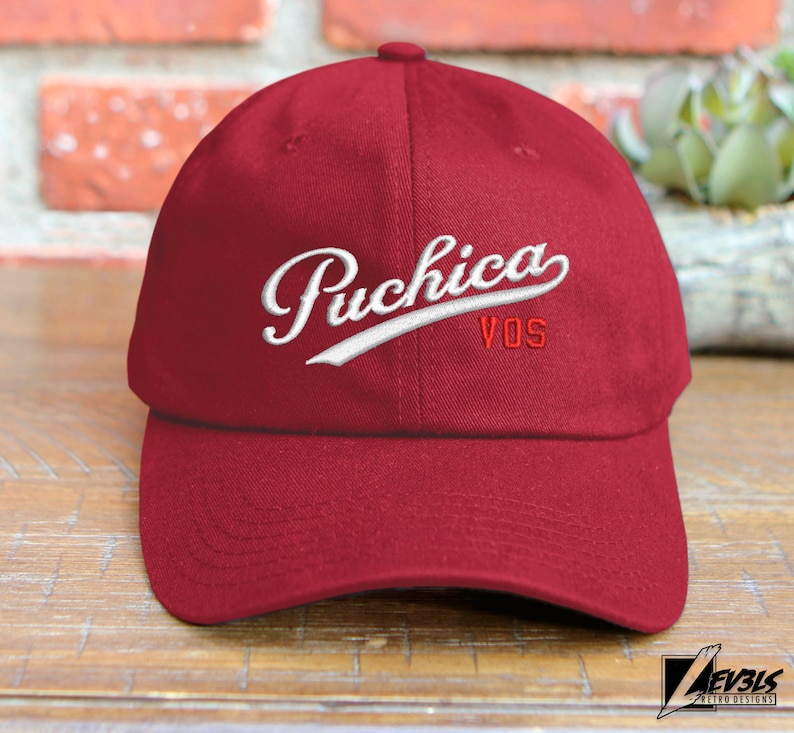 May include: A red baseball cap with a white embroidered logo that says "Puchica VOS".