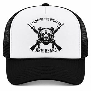 May include: A black and white trucker hat featuring a graphic of a bear head centered between two crossed rifles. The text I SUPPORT THE RIGHT TO ARM BEARS is printed in black capital letters around the central bear and rifle illustration.