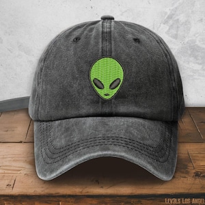 May include: A black denim baseball cap with an embroidered green alien face on the front.