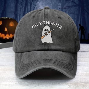 May include: A black distressed baseball cap with an embroidered white ghost holding a rifle and the text "Ghost Hunter".