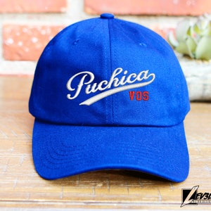 May include: A blue baseball cap with white stitching and the text "Puchica VOS" embroidered in red and white.