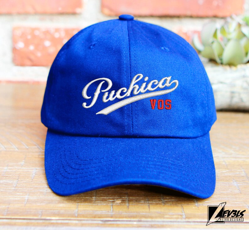 May include: A blue baseball cap with white stitching and the text "Puchica VOS" embroidered in red and white.