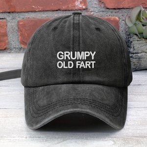 May include: A black distressed baseball cap with white embroidered text that reads "GRUMPY OLD FART".