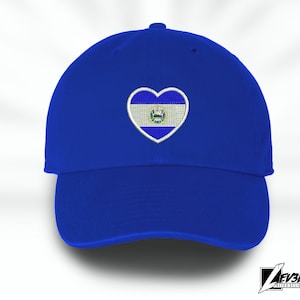 Könnte beinhalten: Eine königsblaue Baseballkappe mit einem gestickten herzförmigen Aufnäher mit der Flagge von El Salvador.