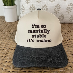 May include: A beige and black baseball cap with the text "i'm so mentally stable it's insane" in brown lettering.