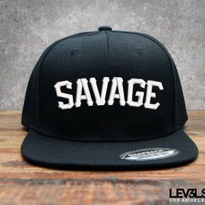 May include: Black and white baseball cap with the word "SAVAGE" embroidered in white on the front.