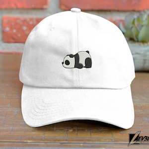 Può includere: Cappellino da baseball bianco con un design di panda bianco e nero ricamato. Il panda è sdraiato sul fianco con la testa girata a sinistra.