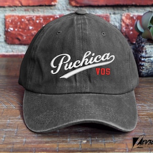 May include: A black baseball cap with a white embroidered logo that says "Puchica VOS".