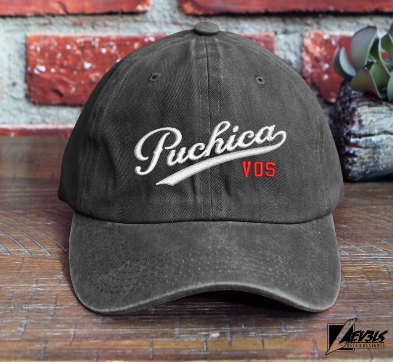 May include: A black baseball cap with a white embroidered logo that says "Puchica VOS".