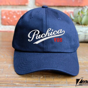 May include: A navy blue baseball cap with a white embroidered logo that says "Puchica VOS".