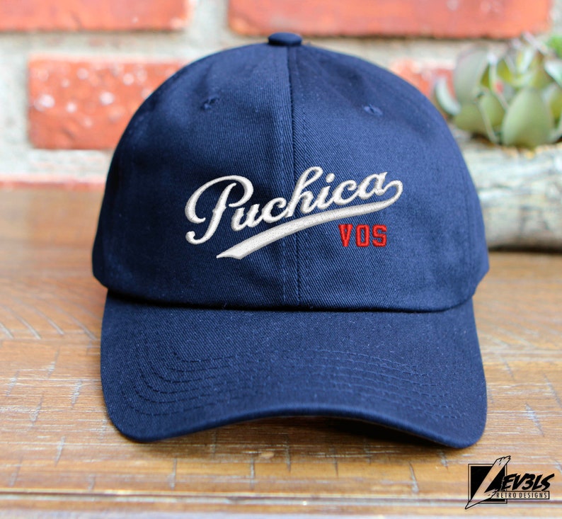 May include: A navy blue baseball cap with a white embroidered logo that says "Puchica VOS".