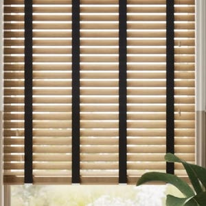 May include: Beige wooden blinds with black tape accents. The blinds are closed, but the light shines through the slats.