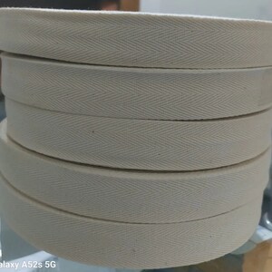 May include: A close-up of a stack of white cotton twill tape with a herringbone pattern. The tape is approximately 2.5 cm wide.