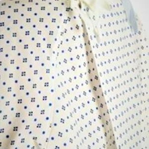 May include: White hospital gown with a blue and white geometric pattern. The gown has a tie at the neck and a tie at the waist.