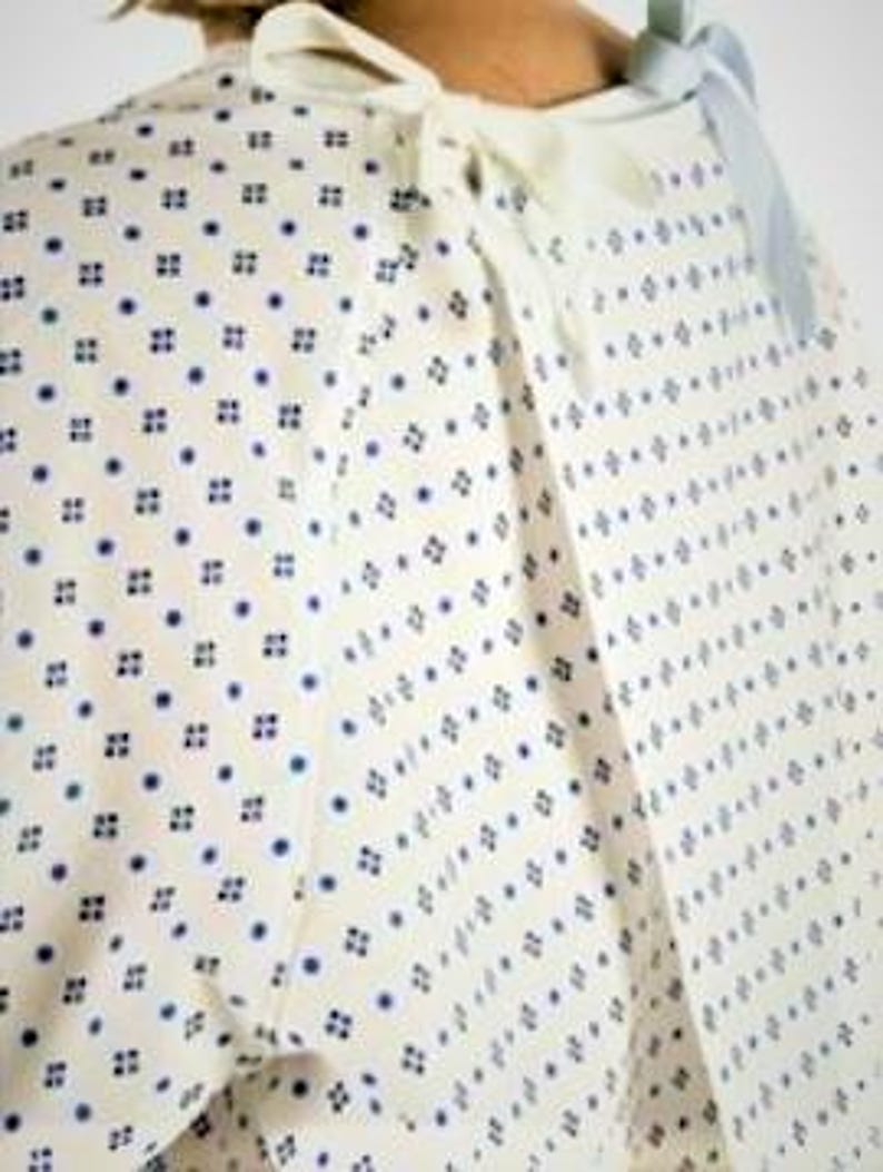 May include: White hospital gown with a blue and white geometric pattern. The gown has a tie at the neck and a tie at the waist.