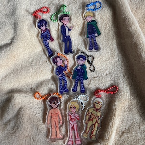 Puede incluir: Ocho llaveros de personajes de anime coloridos con cadenas negras. Los personajes están dibujados en estilo chibi y visten diferentes atuendos. Los llaveros están hechos de acrílico transparente y son perfectos para los fanáticos del anime.