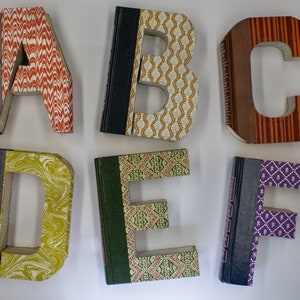 May include: Six book-shaped letters, A through F, made from book covers with different patterns. The letters are arranged in two rows of three.