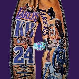 Puede incluir: Un pantal&oacute;n amarillo con ribete de flecos. El pantal&oacute;n est&aacute; cubierto de im&aacute;genes de jugadores de baloncesto que visten camisetas de los Los Angeles Lakers. El texto "LAKERS" y "24" es visible en el pantal&oacute;n.
