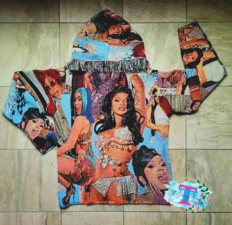 May include: A blue and white hooded sweatshirt with a tapestry design featuring images of women. The sweatshirt has a fringe trim around the hood.