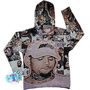 May include: A gray hooded sweatshirt with a collage of images of people, including a large image of a person wearing a pink hat with a racing stripe. The sweatshirt has a drawstring hood and long sleeves.