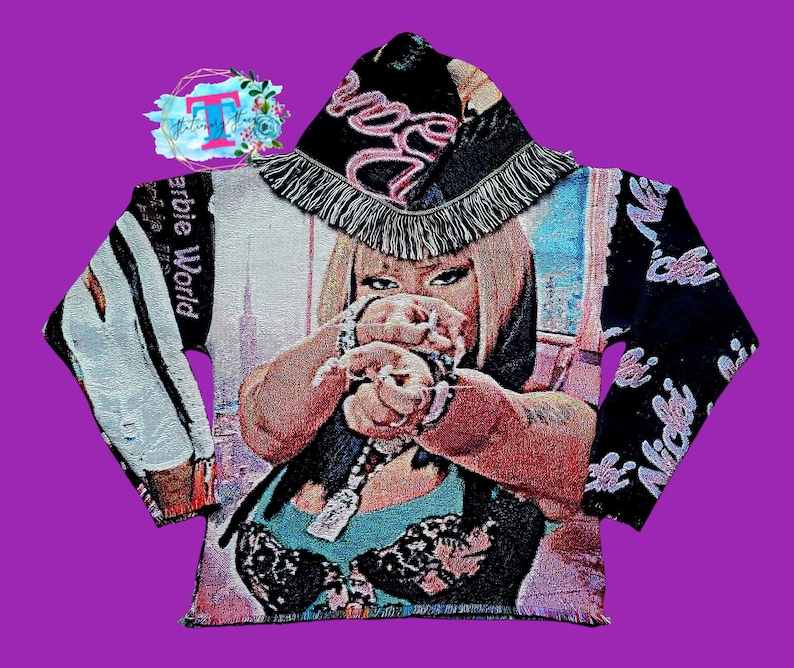 May include: A black and white tapestry hoodie with a pink and white fringe hood. The hoodie features a colorful image of a woman with the text "Barbie World" and "Nicki" on the sleeves.