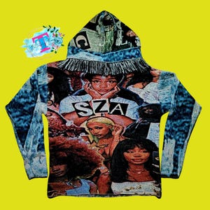 May include: A blue denim hooded sweatshirt with a fringe trim. The front of the sweatshirt features a collage of images of the singer SZA.