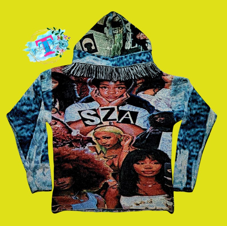 May include: A blue denim hooded sweatshirt with a fringe trim. The front of the sweatshirt features a collage of images of the singer SZA.