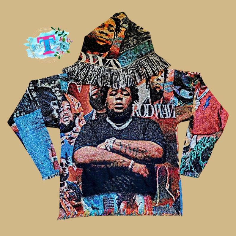 May include: A black hooded sweatshirt with a colorful tapestry design featuring a portrait of Rod Wave. The tapestry design includes a variety of colors and patterns, including blue, red, green, and yellow. The sweatshirt has a fringe trim around the hood and the bottom hem.