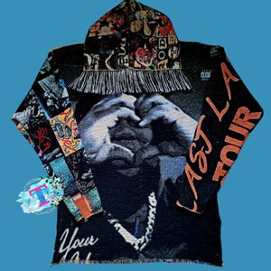 May include: Black hooded sweatshirt with a colorful tapestry design featuring a person making a heart shape with their hands. The sweatshirt has the text "Astroworld" on the right sleeve and "Your" on the bottom left corner.